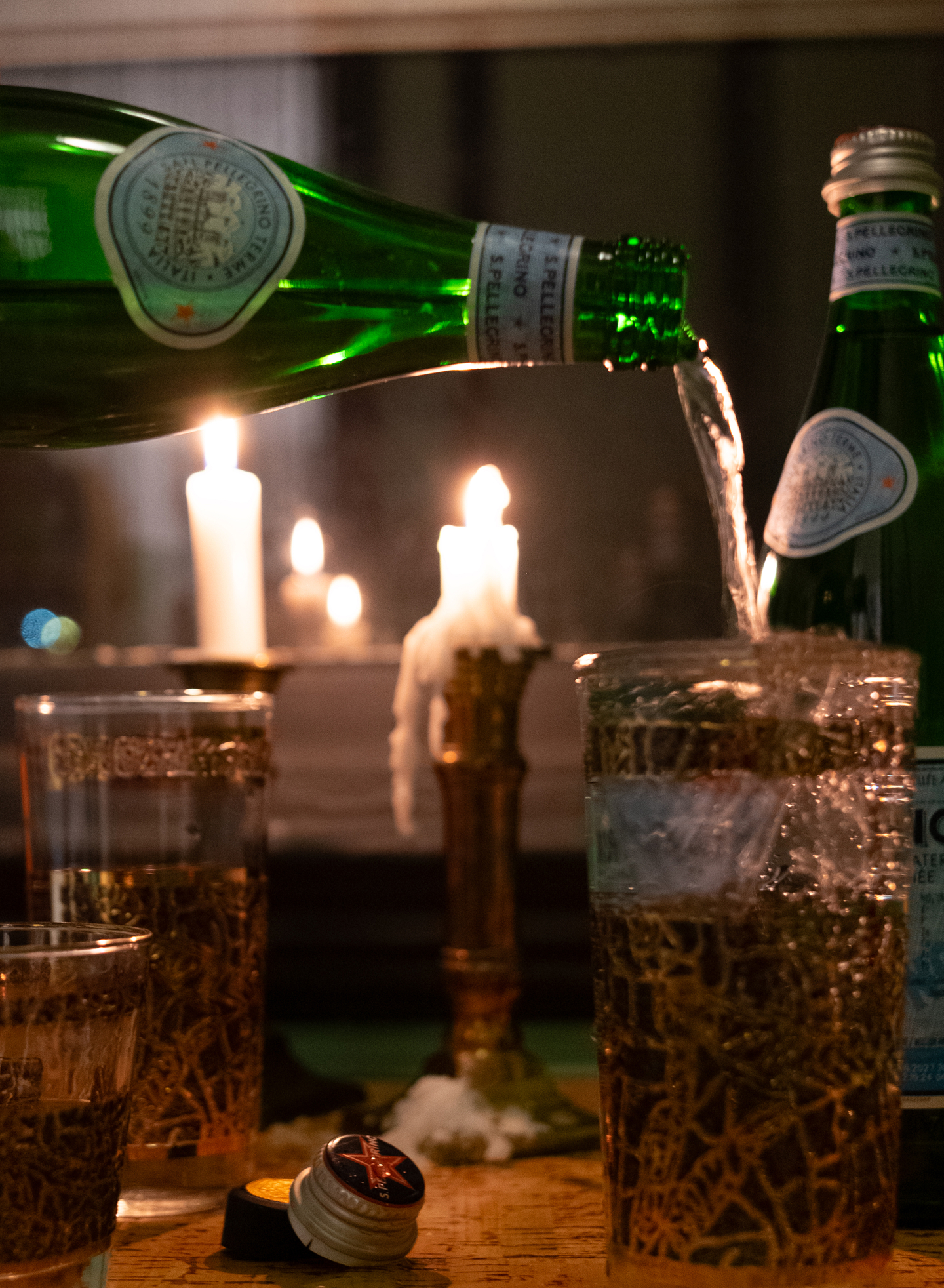 San Pellegrino glass bottle pouring water in a cup on a kitchen table.